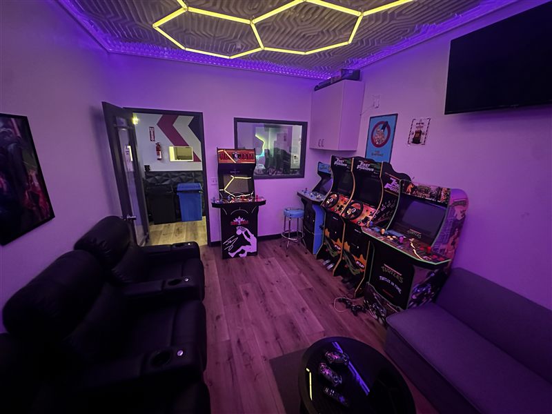 The Arcade Lounge glowing purple, with a row of retro arcade cabinets and lounge seating